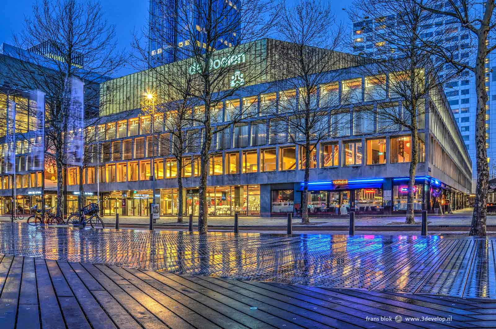 Avondbeeld van concert- en congresgebouw de Doelen in Rotterdam, reflecterend in het vochtige staal en hout van het Schouwburgplein