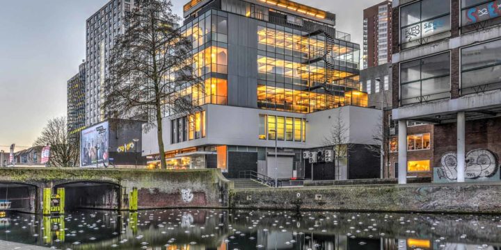 Huf Building, a national monument from the reconstruction era, photographed from the square near Saint Lawrence Church, late in the afternoon, with the building and its lighting reflecting in Delftsevaart