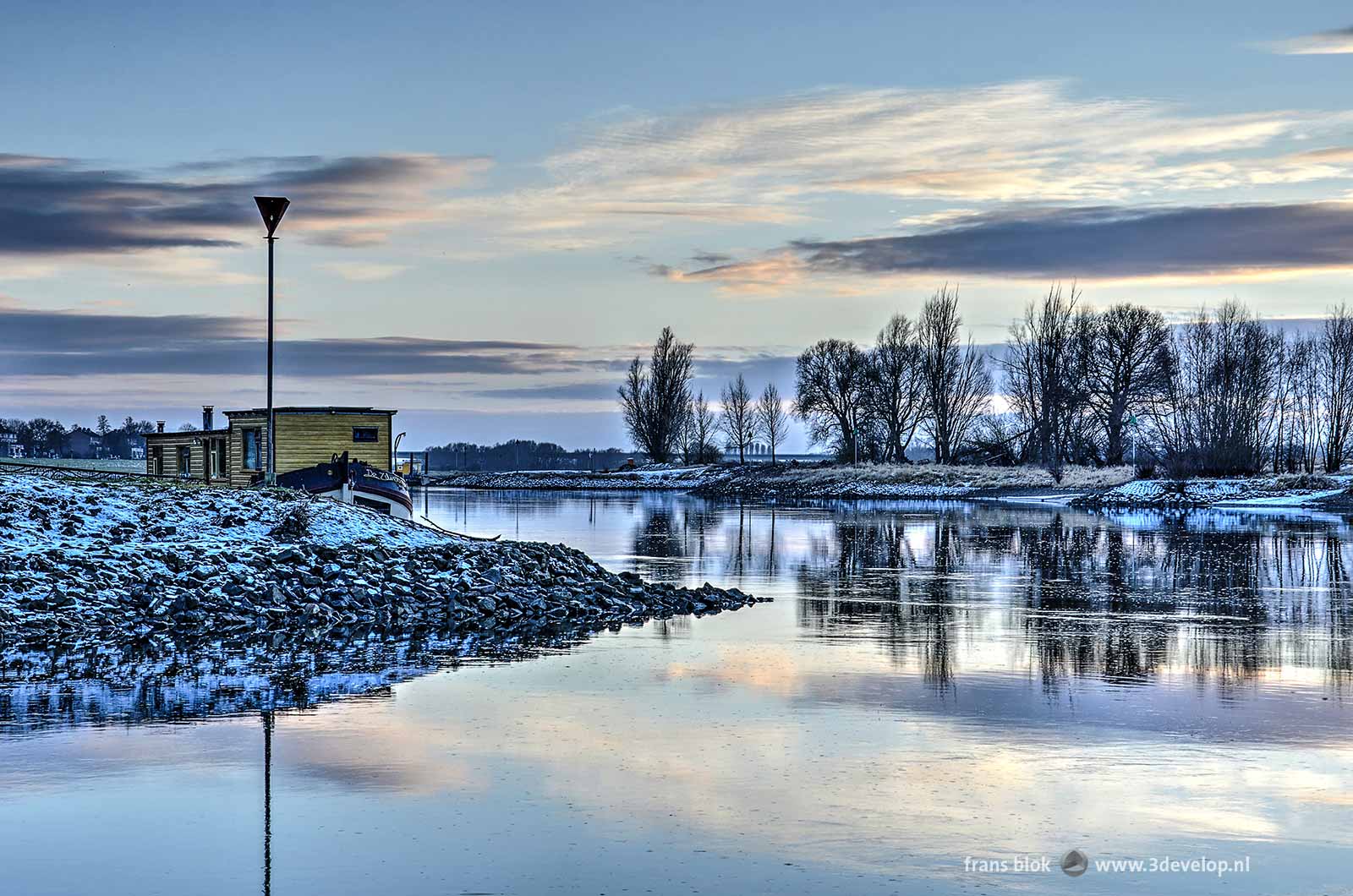 Foto van de IJssel bij Zutphen op een winterse namiddag tegen zonsondergang, met een gele woonboot en sneeuw op de oevers