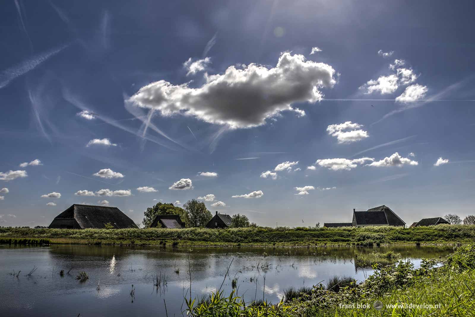 Blue sky with small clouds and contrails above farms on the nature island of Tiengemeten in The Netherlands