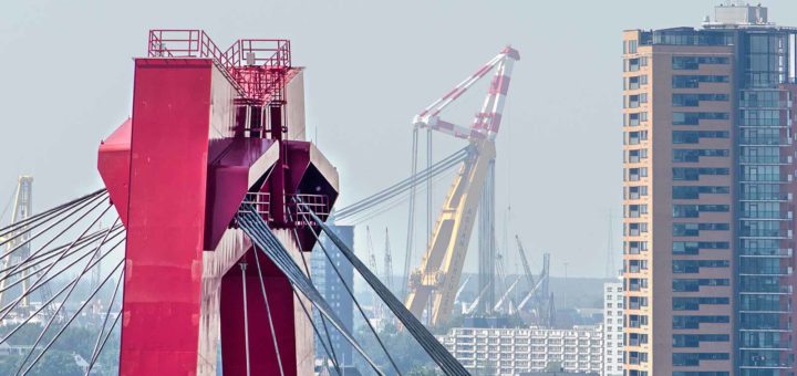 Image made with a telephoto lens showing one of the pylons of willems Bridge in Rotterdam with in the background a residential tower and a large crane in the harbour