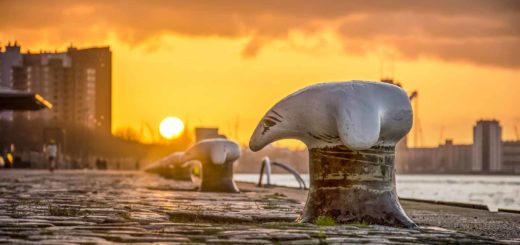 Close-up van een bolder tussen de kasseien op de kade van de Wilhelminapier in Rotterdam met op de achtergrond een vuurrode zonsondergang boven Charlois