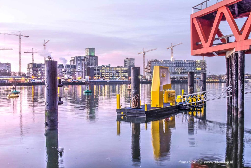 Rijnhaven harbour in Rotterdam with a yellow jetty and a red truss of the New Luxor theatre during sunrise, with the grainsilo and the Fenixlofts at Katendrecht in the background