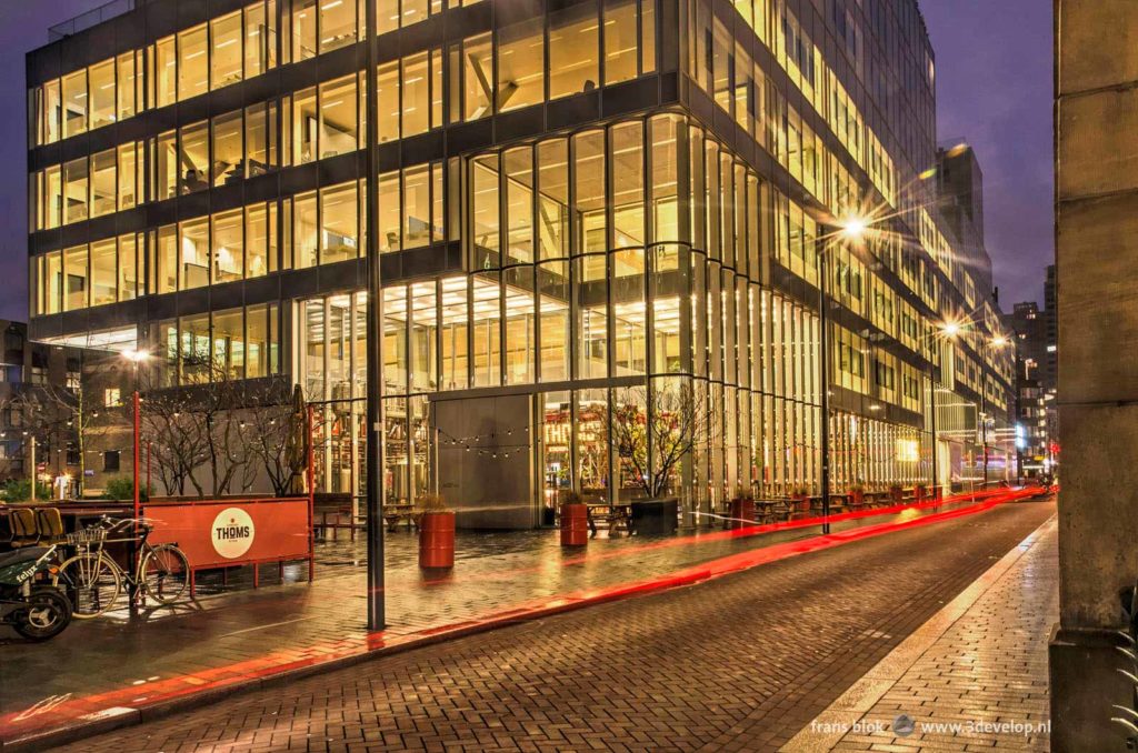 Red light trail created by a bicycle in a street near the Timmerhuis mixed-use building in Rotterdam on a rainy morning