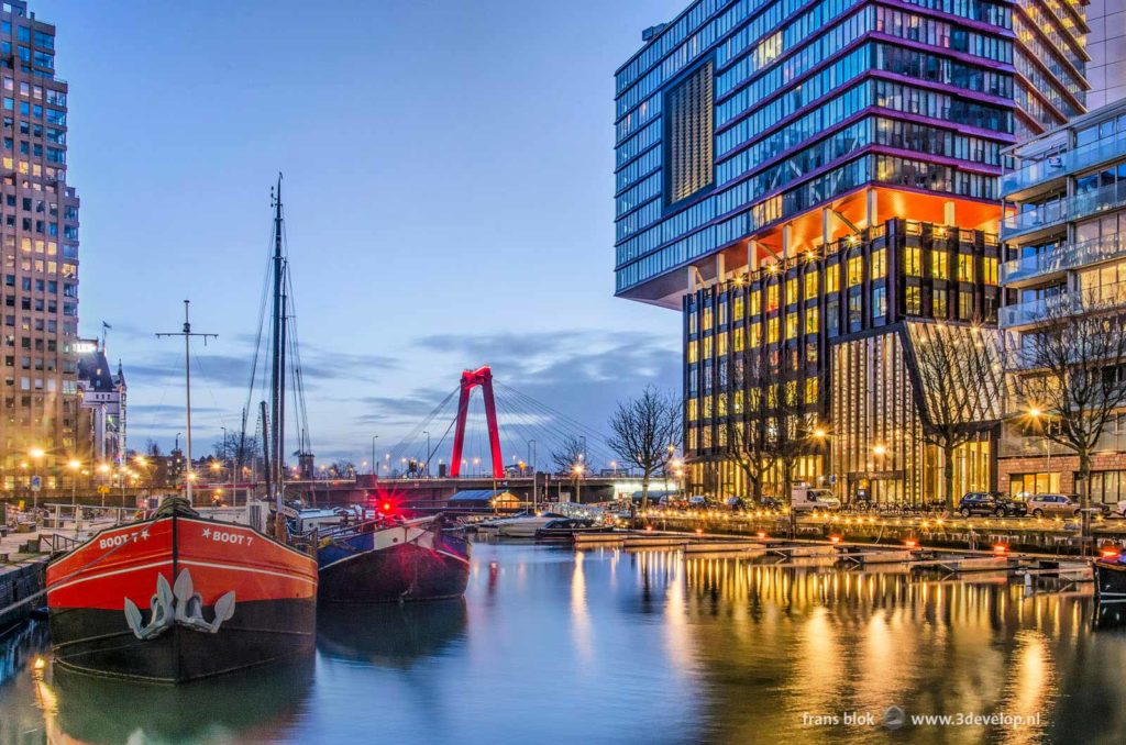 Wijnhaven harbour in Rotterdam with residential building The Red Apple, some historic barges and in the background Willems bridge during the blue hour before sunrise