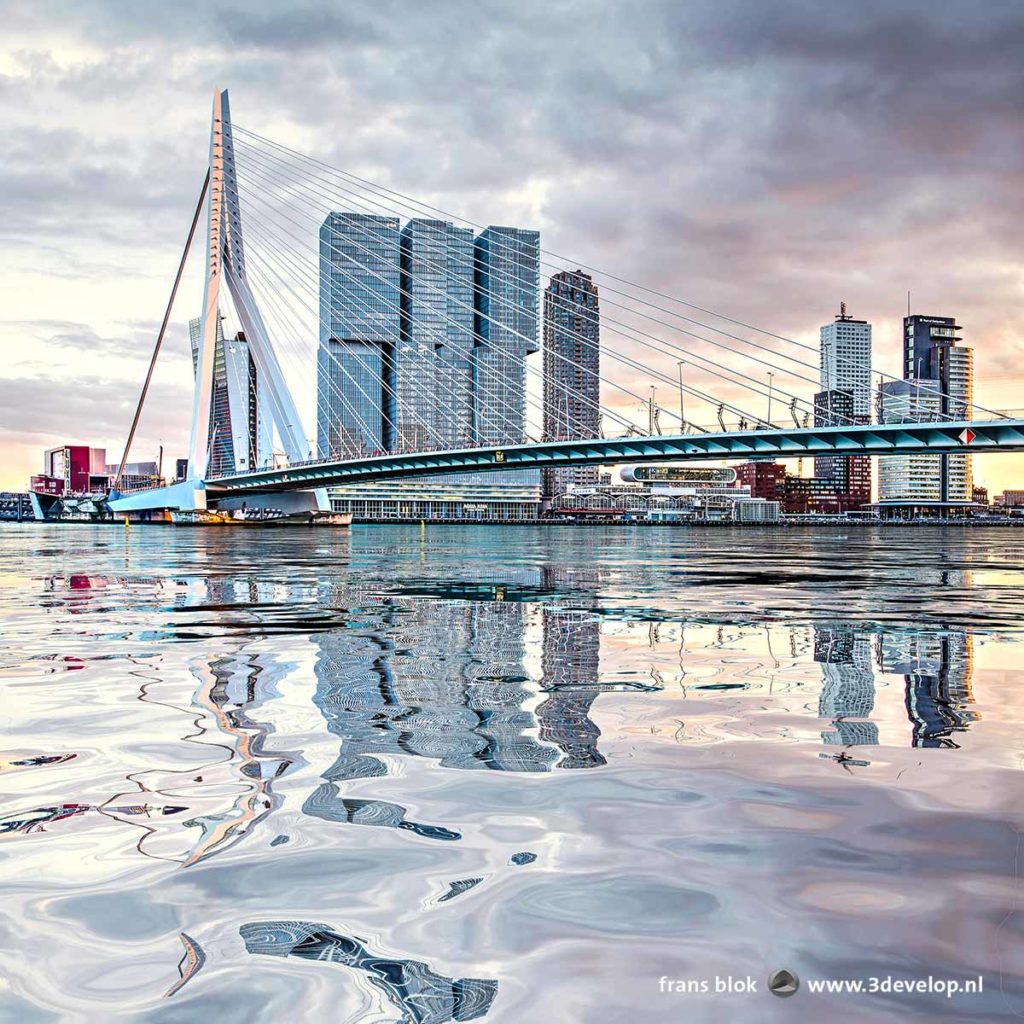 Erasmus Bridge and Wilhelmina Pier in Rotterdam, The Netherlands, under a dramatic evening sky, reflecting in a digitally generated water surface