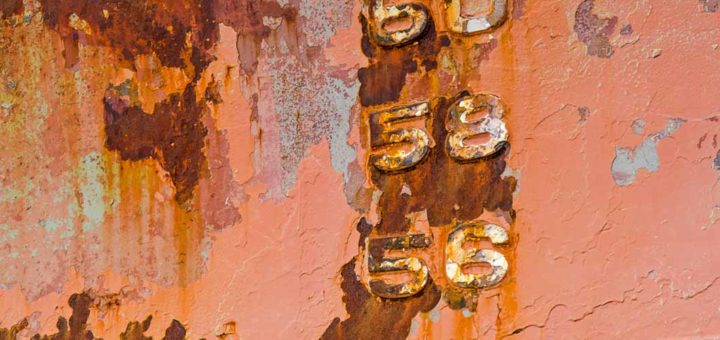 Details of a ship hull with peeling paint, rust stains and stripes and embossed numbers of the draught mark