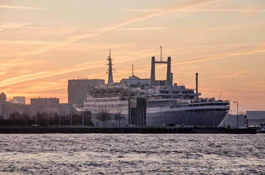 Former cruise ship SS Rotterdam, the eneba grain silo and the Nieuwe Maas river in Rotterdam at sunrise under a beautiful sky with contrails