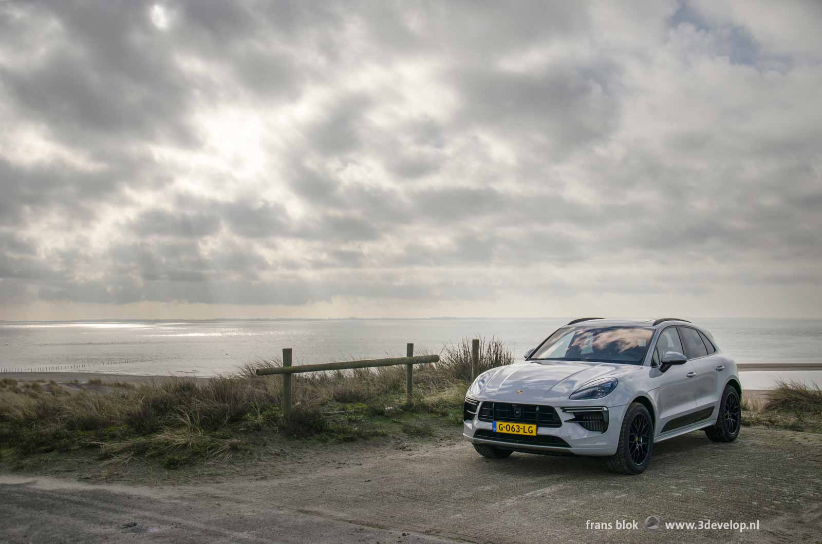 Silver grey Porsche Macan Turbo parked at Maasvlakte near Rotterdam with the sea and a spectacular cloudy sky in the background