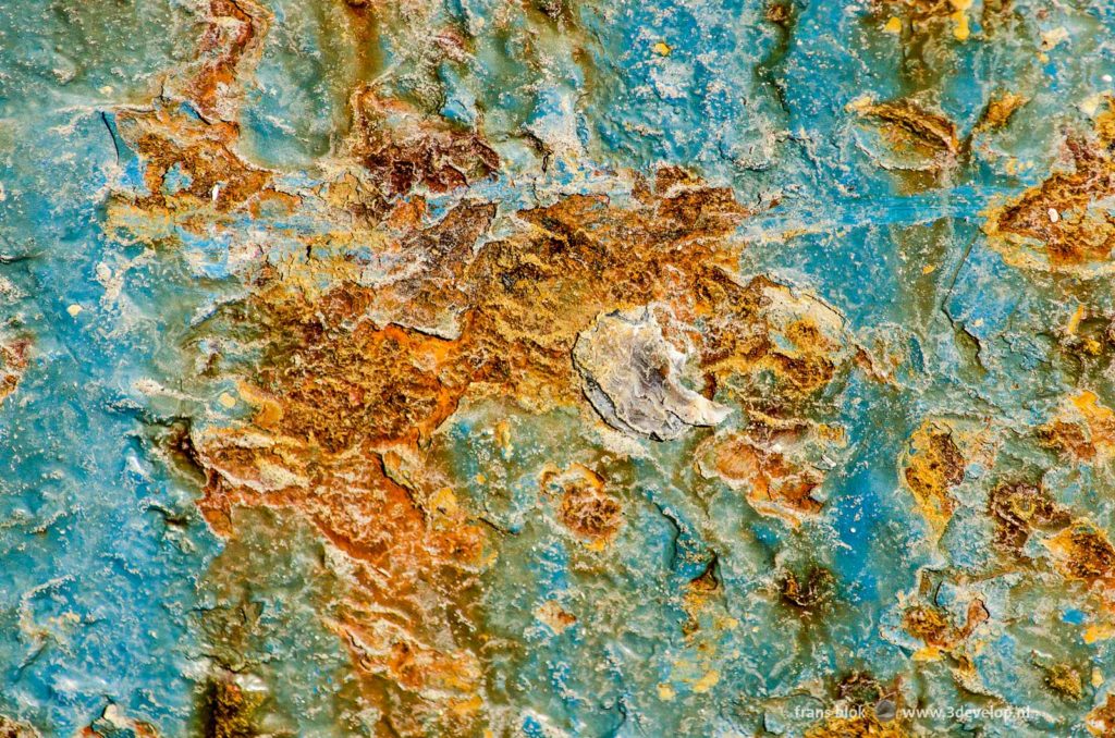 Detail of a light blue steel ship's hull that is heavily damaged by rust