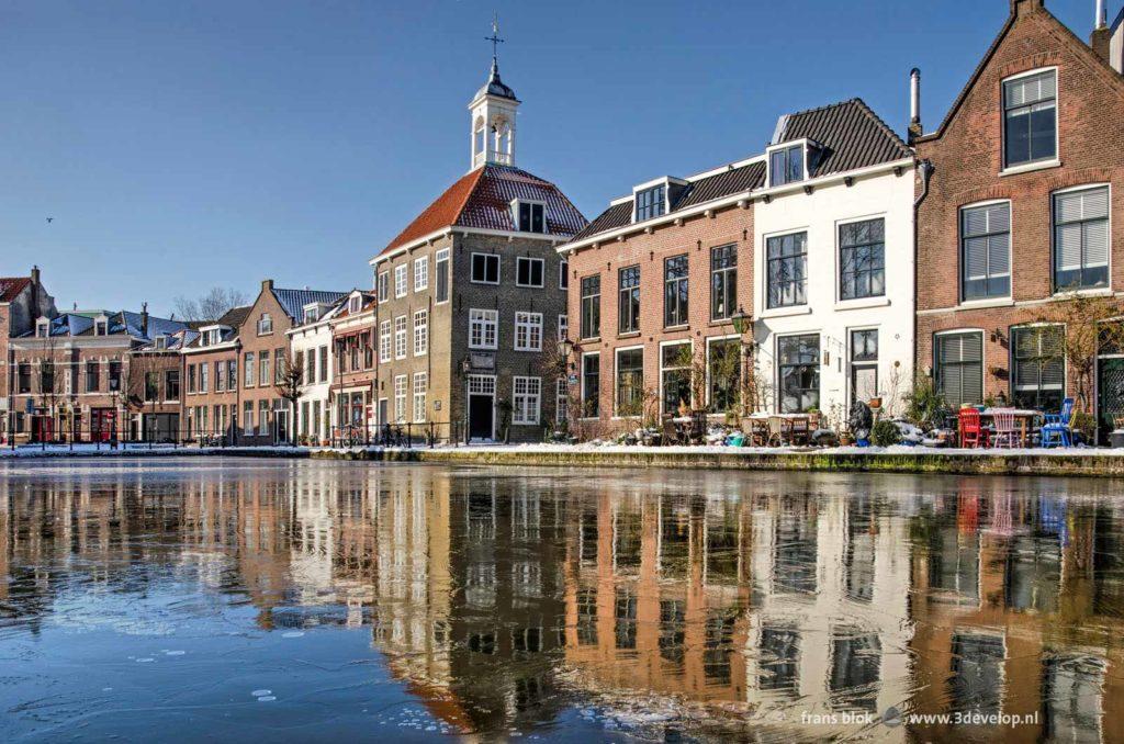 The Bag Carriers house and other historic buildings reflect in the thin ice on Schie river in Schiedam, The Netherlands on a sunny day in the winter of 2021