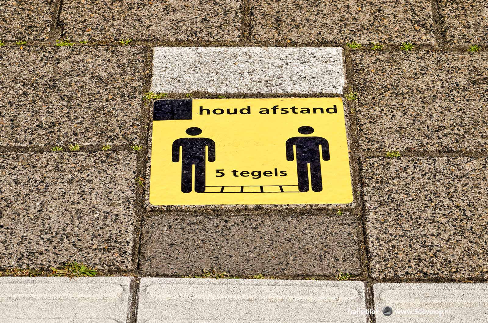 Pavement tile on Dutch railway platform asking to keep 1,5 metre, or vijf tiles, distance, because of covid-19