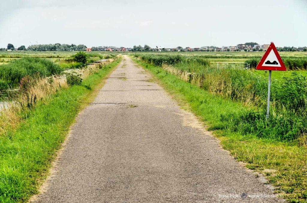 Landweggetje in de dichtbevolkte Rijnmond, tussen drassige weilanden in de Bergboezempolder in Lansingerland met nieuwbouwwijk Berkel Westpolder aan de horizon