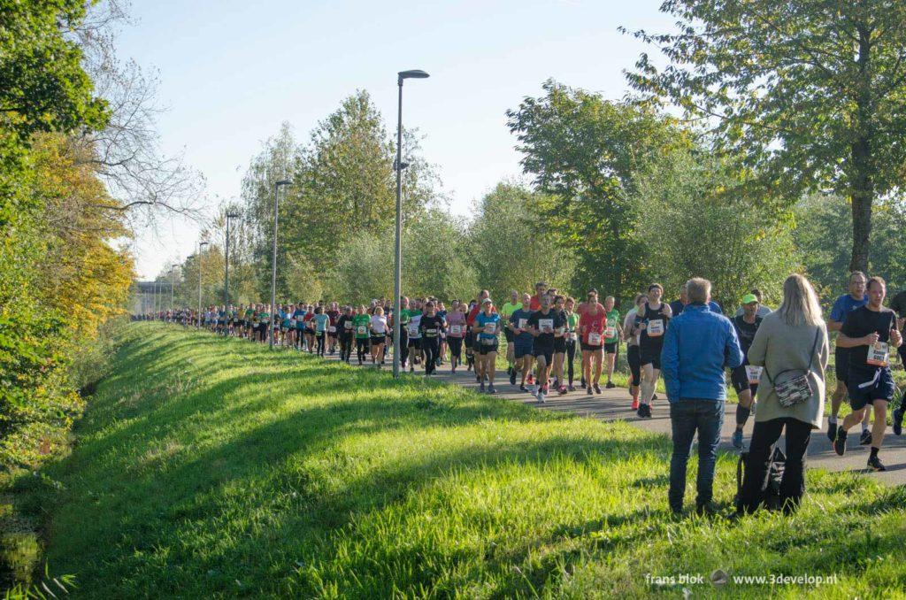 Twee spectactors watch hundreds of runners on a path in green environment during the 2021 Rotterdam marathon