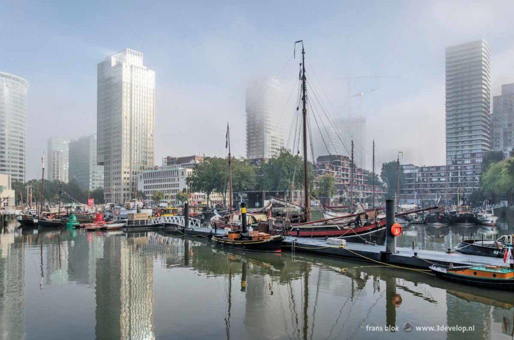 Leuvehaven harbour in Rotterdam, Holland, with historic vessels and modern highrise buildings on a foggy day in autumn