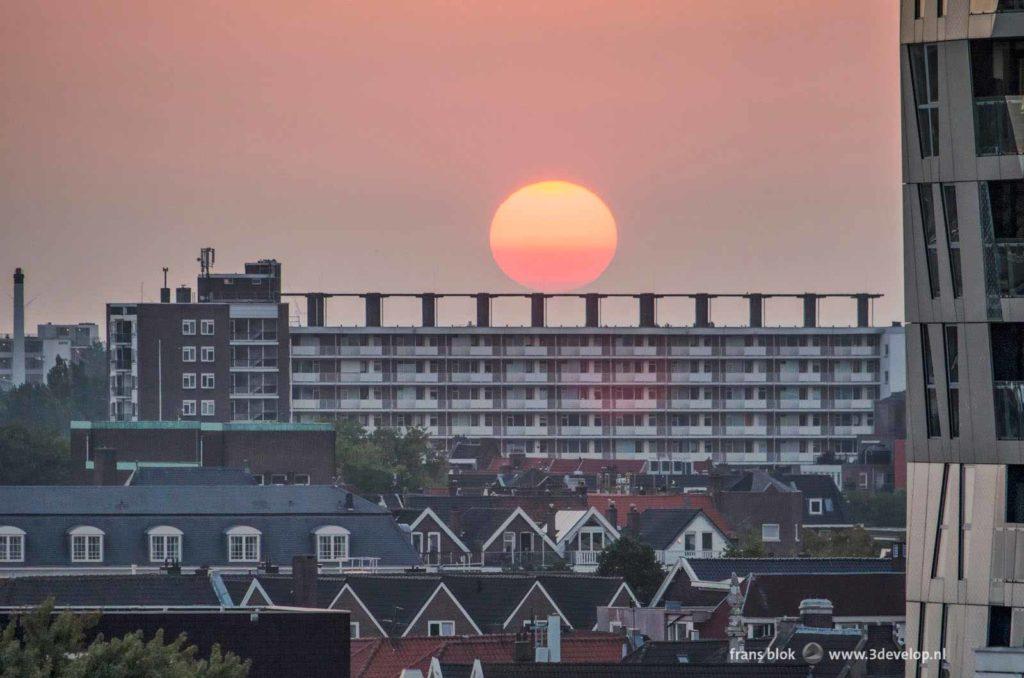 The setting sun seems to rest on a concrete construction on the roof of a modernist residential building in Rotterdam, The Netherlands