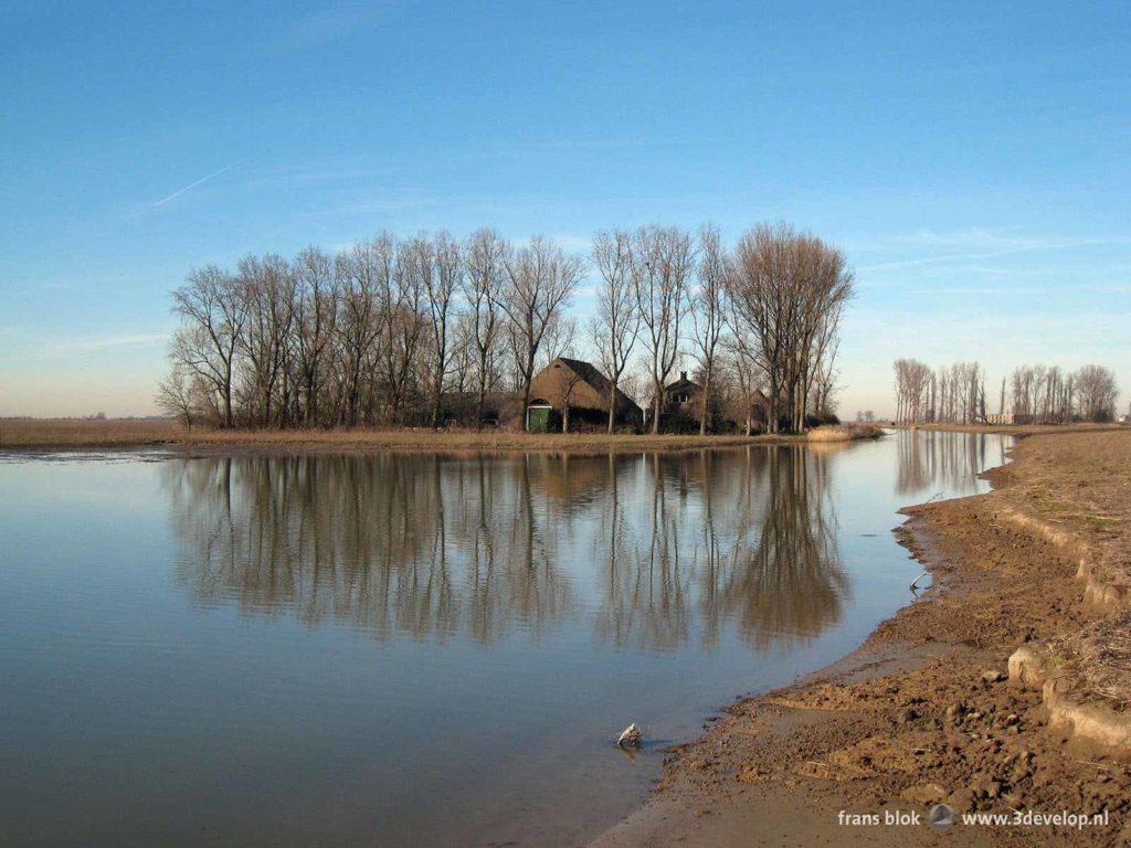 An old farm and adjacent buildings reflect in the still waters of a creek on the nature island of Tiengemeten in the Netherlands