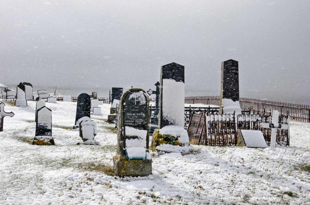 De zon breekt door de wolken tijdens een sneeuwbui boven het kerkhof op het eiland Flatey in IJsland