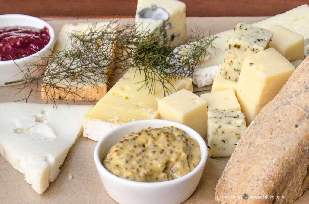 A wooden plate with bread, various cheeses and mustard