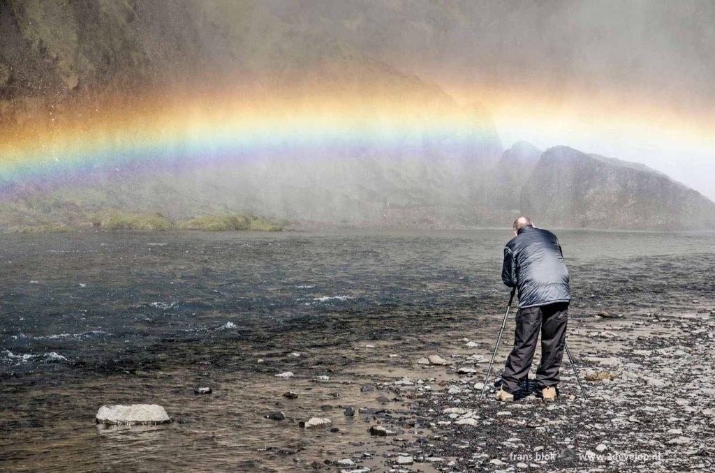 Photographer with tripod capturing rainbow at Skogasfoss waterfall in Iceland, from the top 10 of best photos of 2022