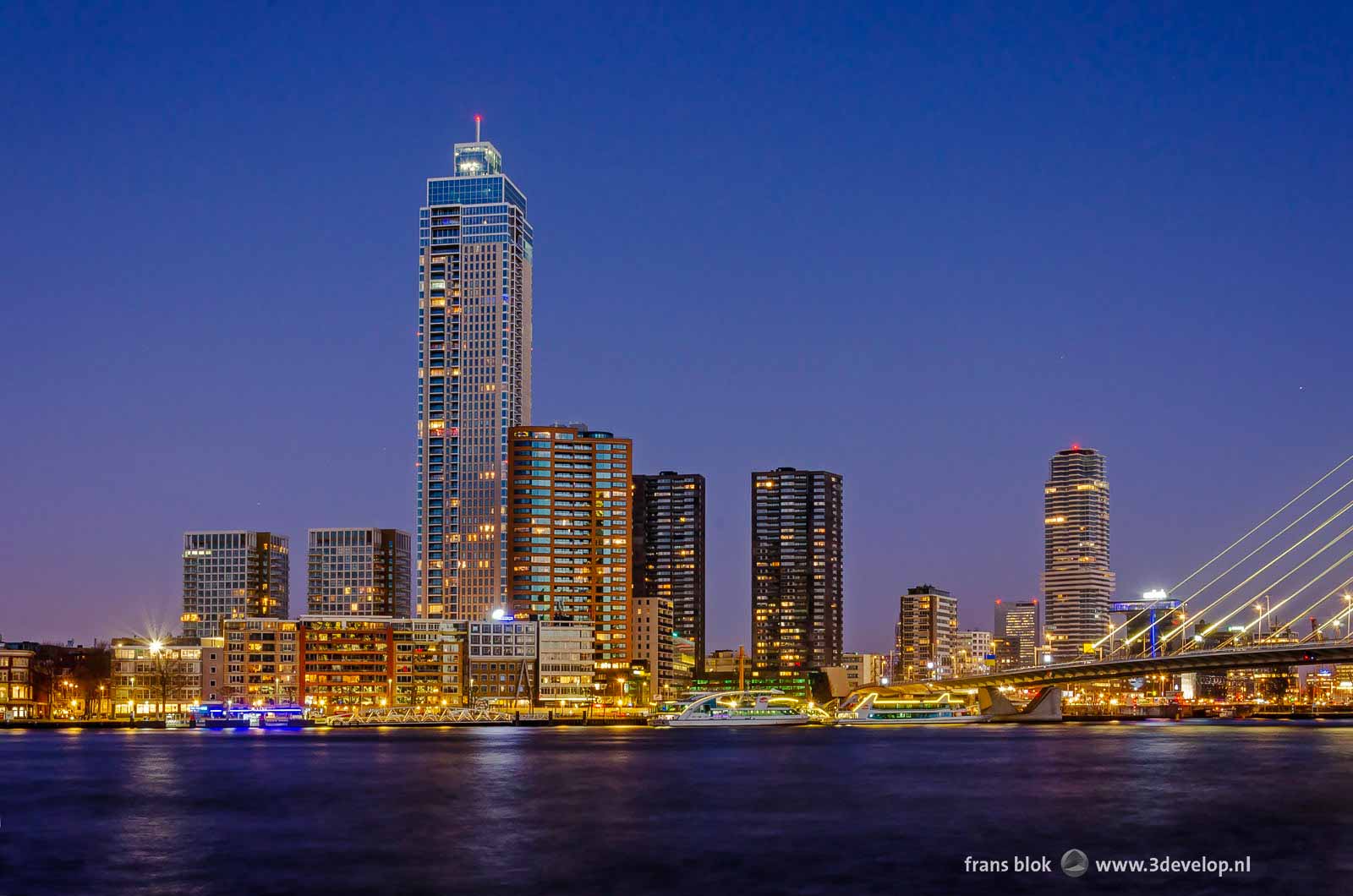 The Nieuwe Maas river in Rotterdam with onder other side Zalmhaven tower and some lower buildings and a piece of Erasmus Bridge in the blue hour on a morning in January