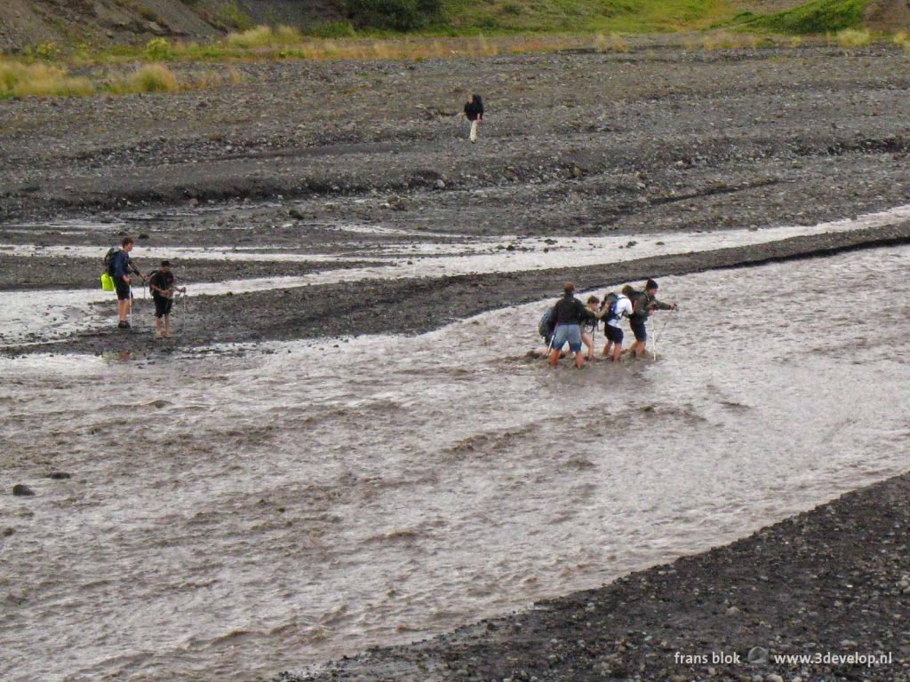 Hikers with sticks and backpacks cross a river with some effort near Thorsmork in Iceland