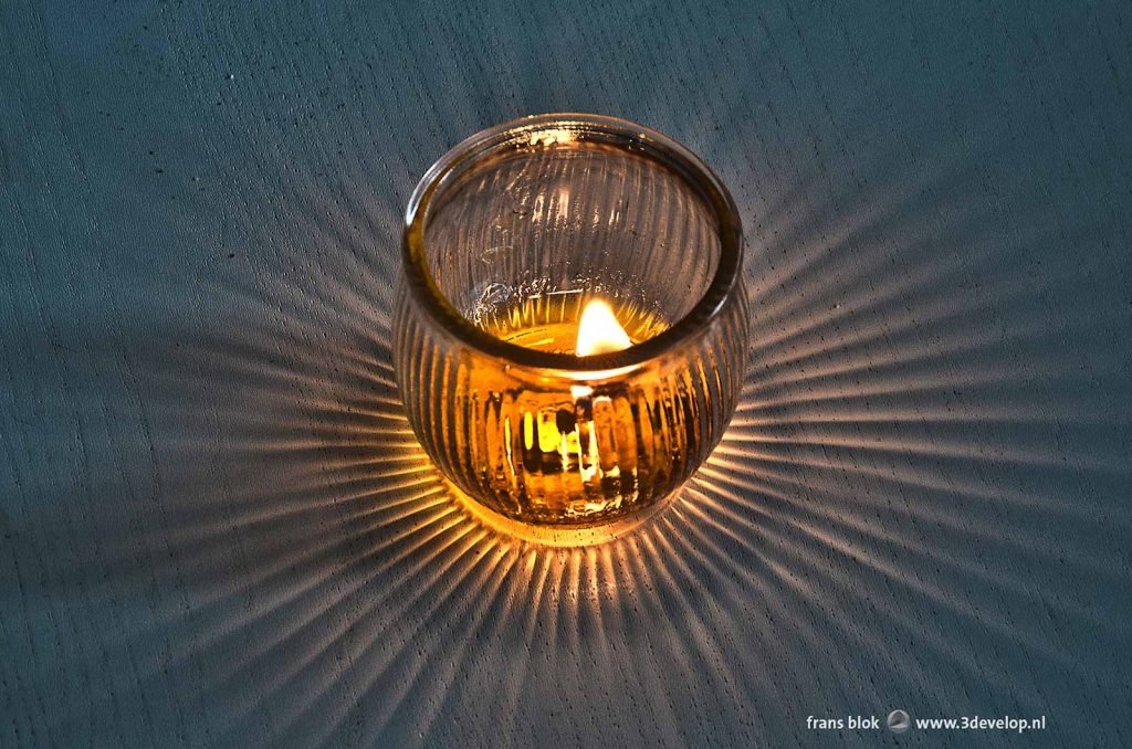 Glass candle holder with burning flame and rays of light in all directions