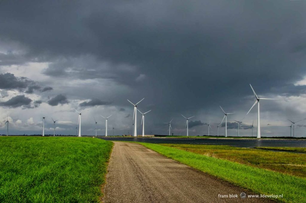 Asphalt road on a dijk on Sint Philipsland, Zeeland, The Netherlands with in the background wind turbines under a dramatic sky