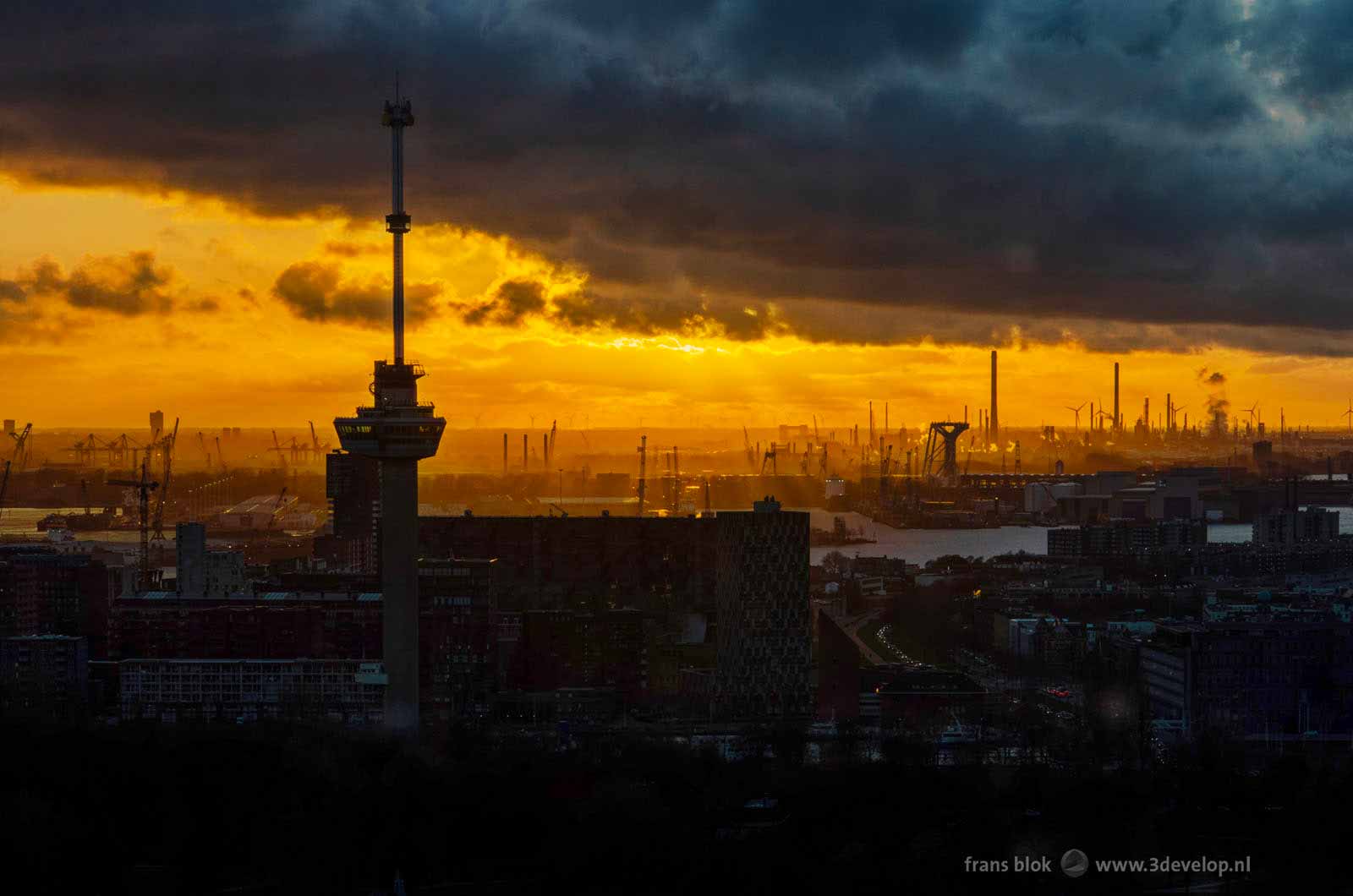 De zon gaat vlammend onder in de Rotterdamse haven achter de Euromast