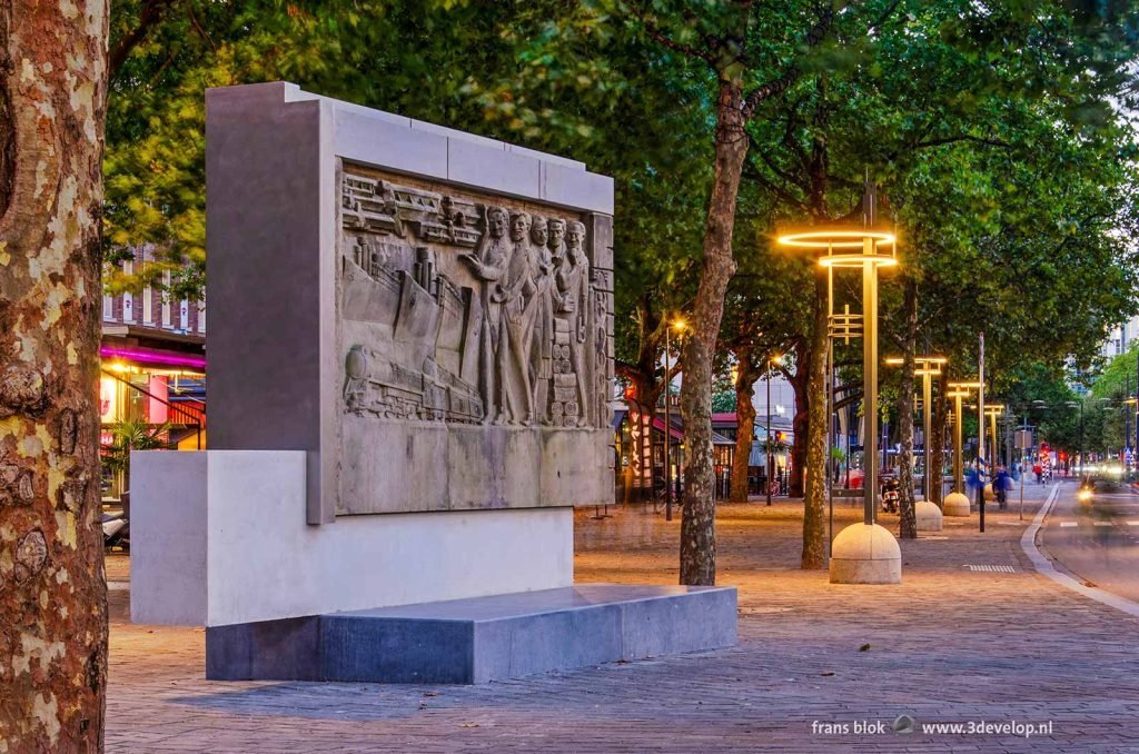 Coolsingel boulevard in Rotterdam during evening twilight, with the sculpture from the old Bijenkorf department store, art deco lamps and a lush canopy of plane trees