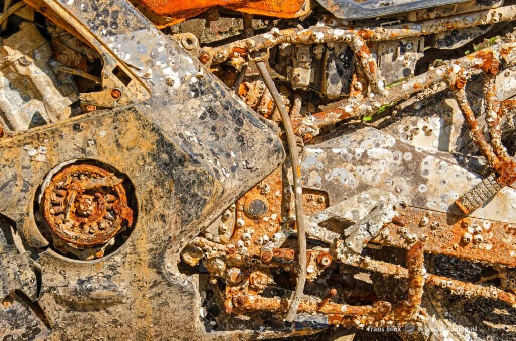 Close-up van een uit het water opgeviste motorfiets, met roest, vuils, krasse en kleine schelpjes