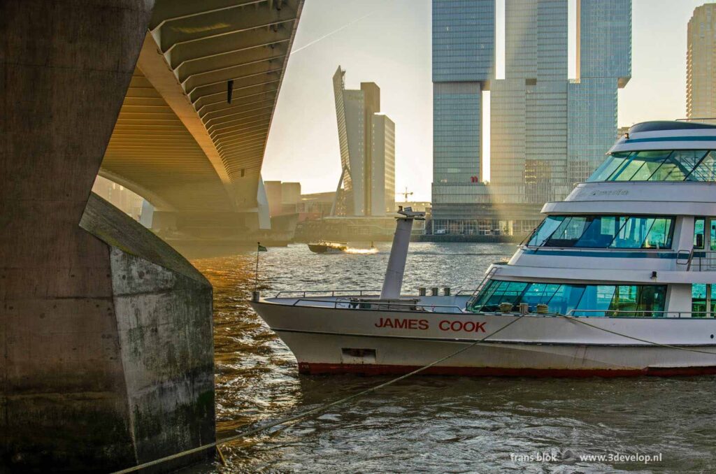 Zicht vanaf de kade op de Nieuwe Maas, een Spidoboot, de Erasmusbrug en een watertaxi tijdens het gouden uur