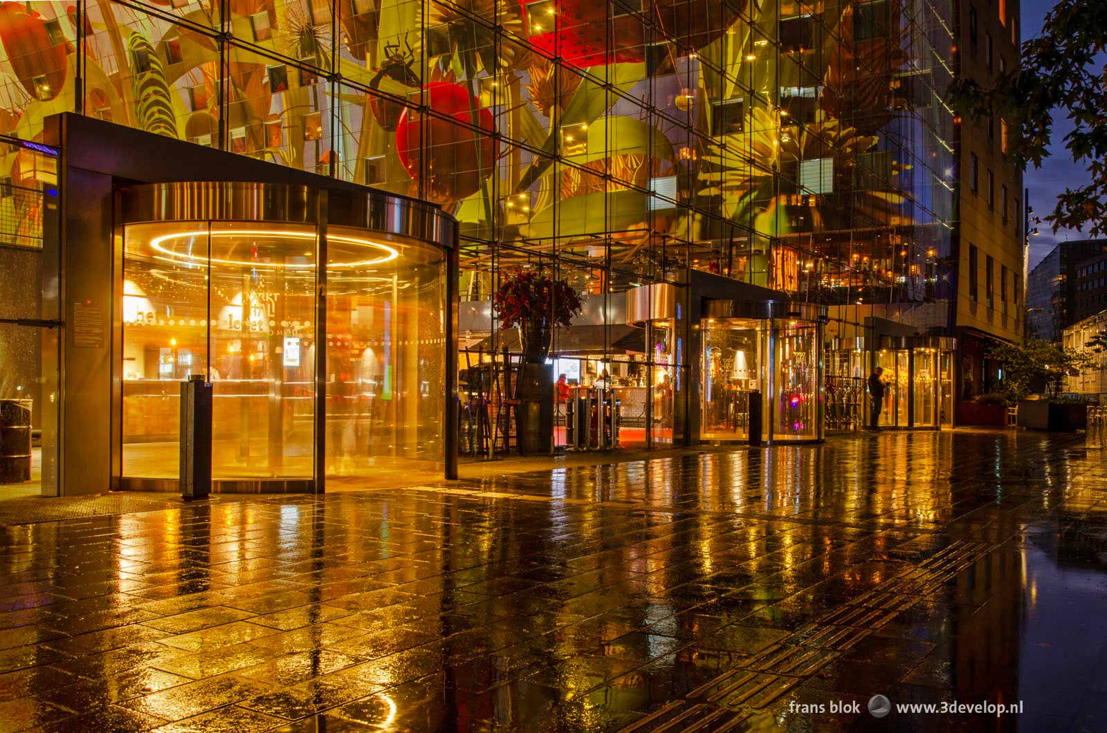 Het interieur en kunstwerk van de Markthal in Rotterdam weerspiegelt in de natte bestrating tijdens de avondschemering